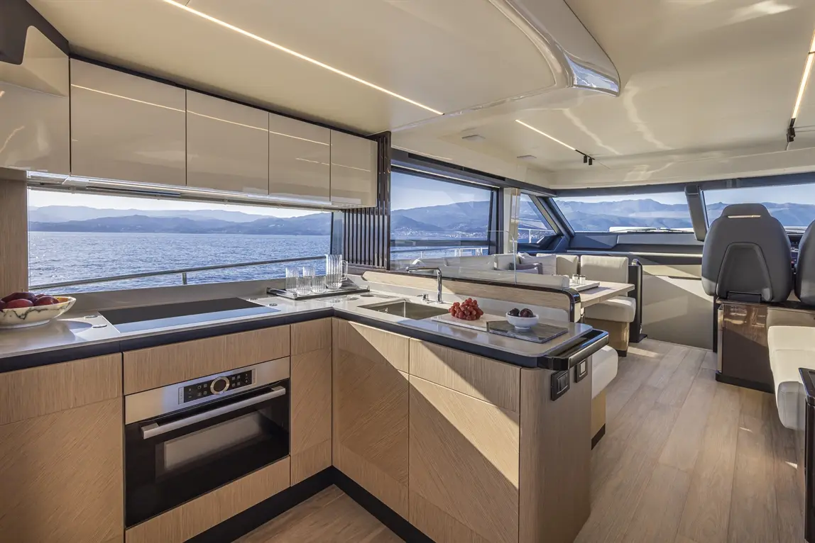 Modern yacht interior featuring a sleek kitchen, dining area, and panoramic sea views, with fruits on the counter.